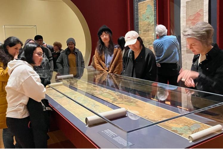 A group of people gather around a glass-encased scroll in a museum