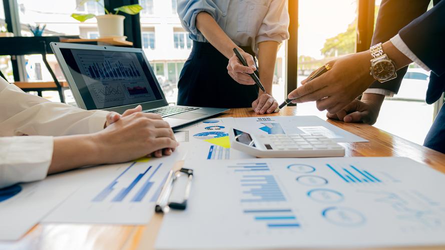 A group of business professionals meeting to analyze data for a marketing plan on a table with graphs and a laptop with a calculator.