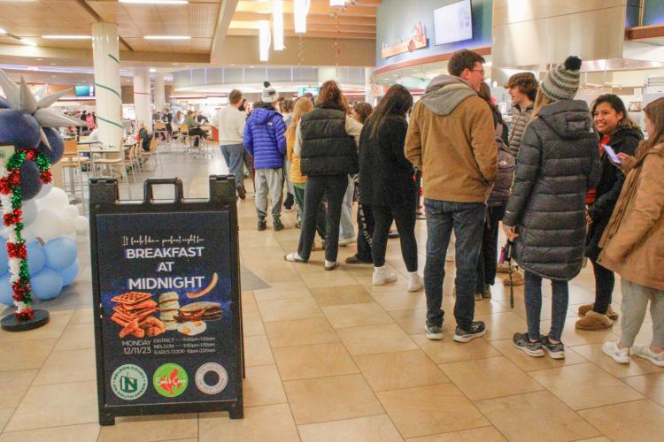 Students line up at a dining hall, with a "Breakfast at Midnight" sign in the foreground