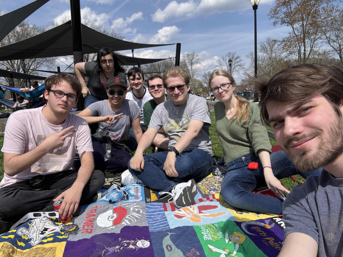 A group of people pose for a selfie, seated on a picnic blanket