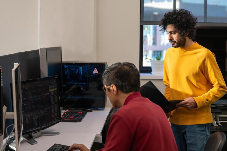 One person working on computer code as another watches, holding a laptop at Ohio University.