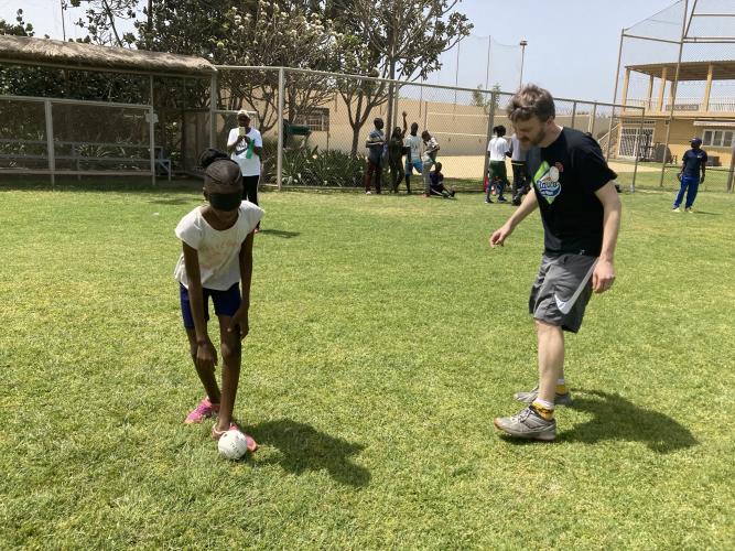 Standing on a baseball field, a man instructs a student who is wearing a blindfold