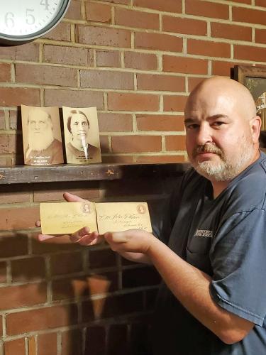 Image of Chris Sauders holding letters in front of two photos on mantle