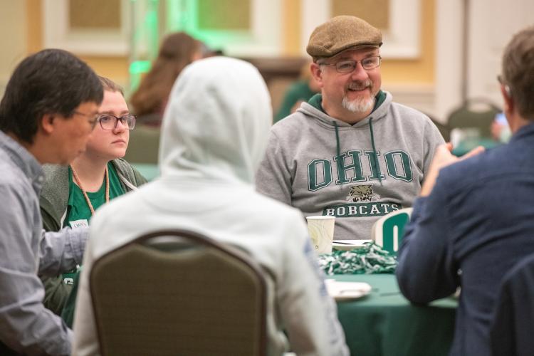 A father wearing an Ohio University sweatshirt sits with family members and others at the Pancakes with the President breakfast during Dads Weekend 2023