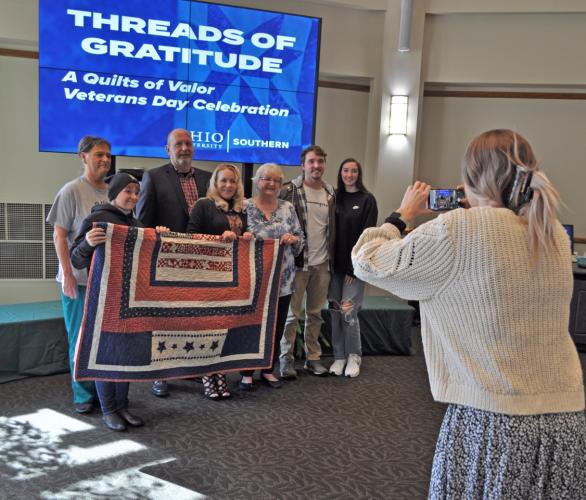 woman taking photo of seven family members behind Quilt of Valor