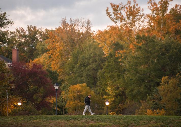 A student walks on OHIO's Athens Campus on a Fall day when the trees are filled with colorful leaves