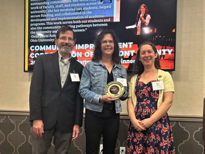 woman holding an award in center of photo featuring 3 people