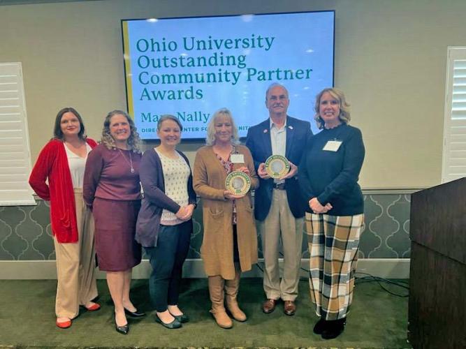 six people hold two awards at the front of a room