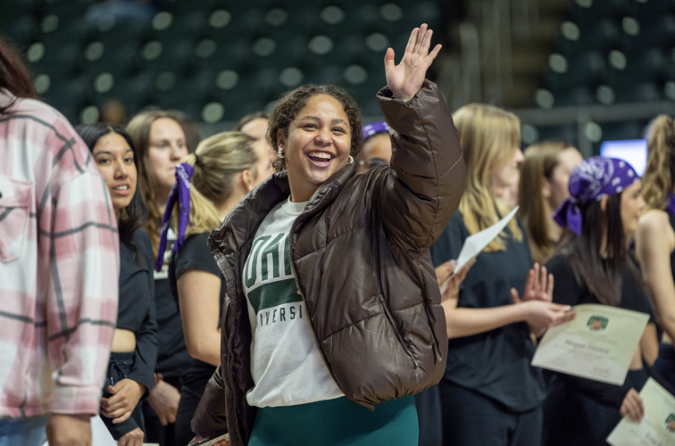 An OHIO student is shown waving to a friend while surrounded by other students in the Convocation Center