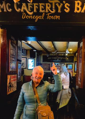 Maureen Weissenrieder, smiling, poses beneath a sign for McCafferty's Bar in Donegal Town