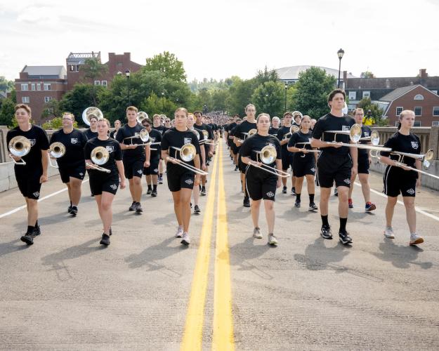 Marching 110 band members march up a brick street holding their instruments