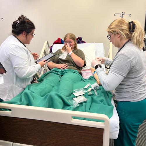 Two nursing students attend to simulation patient with breathing mask