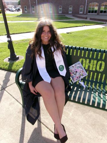 Young woman sits on bench in graduation smock