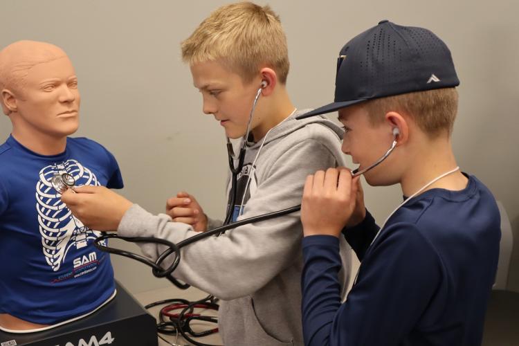 Two students wear stethoscopes and put them on a dummy at the STEM Discovery Day event