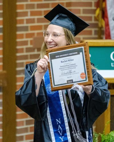woman in cap and gown holding plaque and smiling
