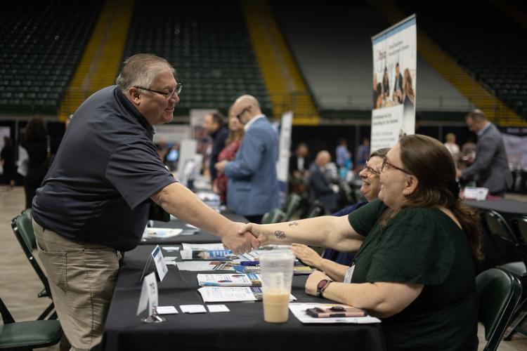 A man shakes hands with two people sitting at a booth at the Ohio Business Matchmaker event