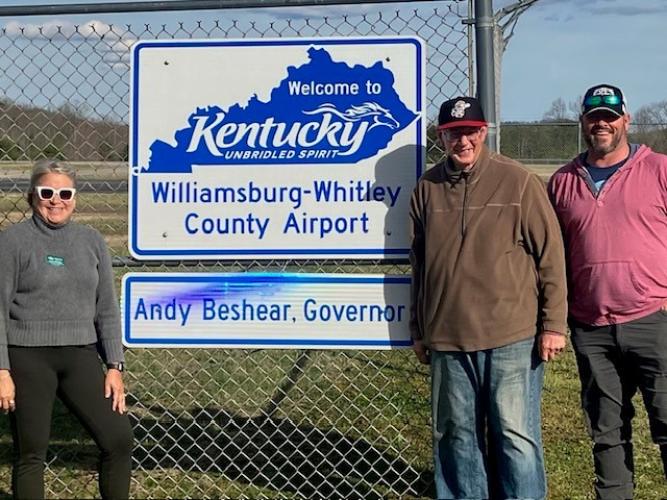 Laurie McKnight, Brent Lane and another individual stand outside, in front of the Williamsburg-Whitley County Airport sign in Kentucky