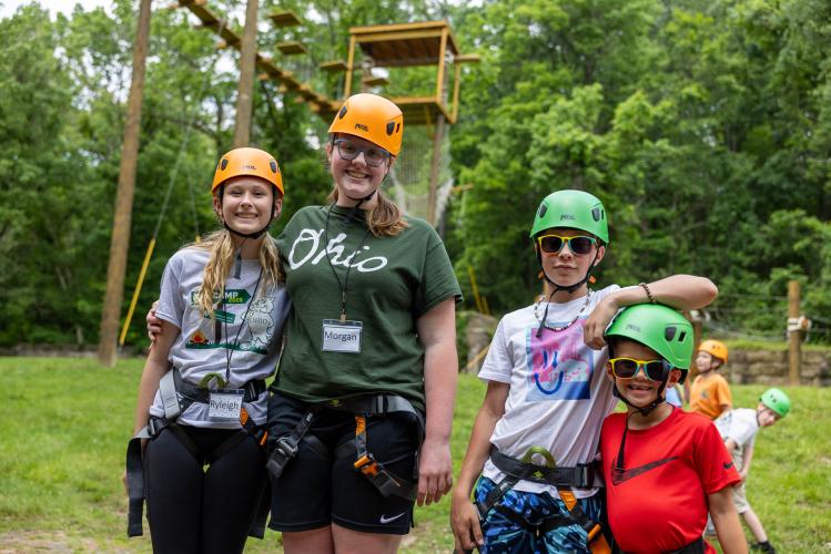 Participants at Cat Camp smile together for a photo outside while wearing helmets for the ropes course