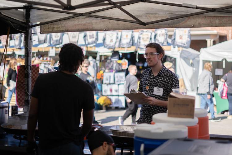 Ryan Humeniuk asks research questions to worker in a booth at an outdoor festival