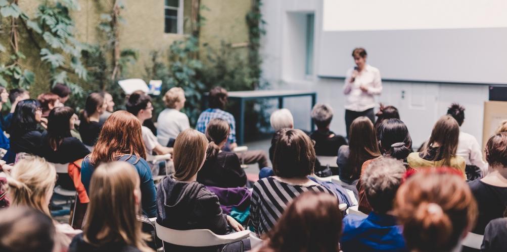 A professor teaches while standing in front of a class of students