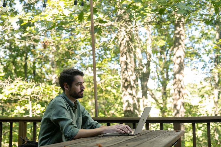 A man works on a computer while sitting at a table outside