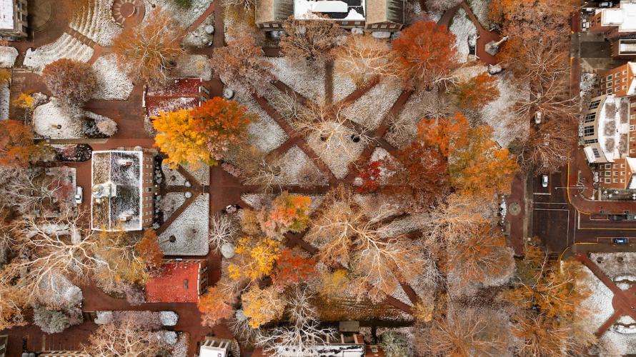 The College Green is shown with snow on the ground and colorful Fall leaves on the trees in this aerial image.