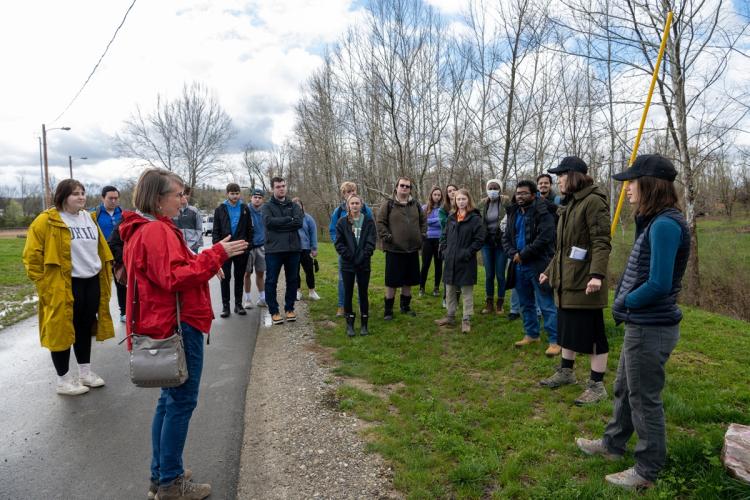 An OHIO faculty member talks to a group of students while standing outside on a paved bike path or small road, while some students stand in the grass