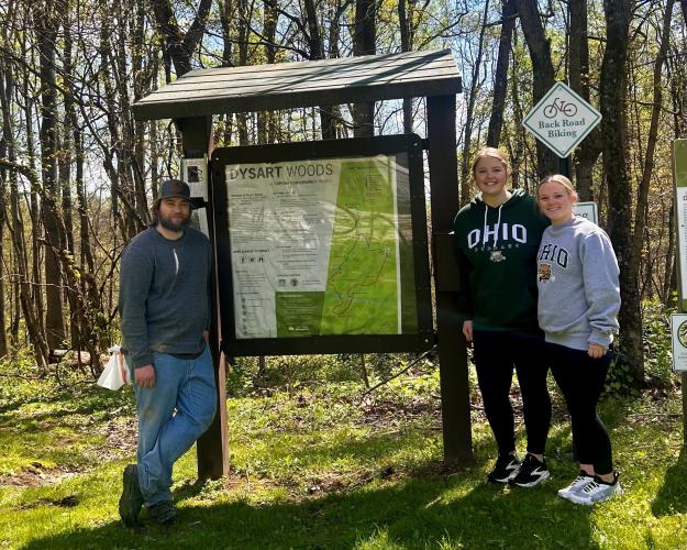 Photo of 3 people standing next to a sign at the entrance of Dysart Woods:  Marshall Dyer, Sophia Withrow, Kiara Triplett