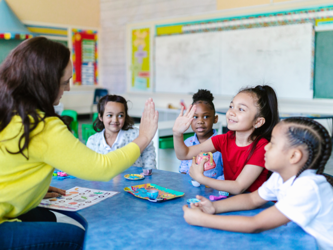 teacher at small table with elementary students giving a student a high five