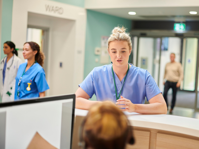 healthcare worker standing at desk talking to woman on computer