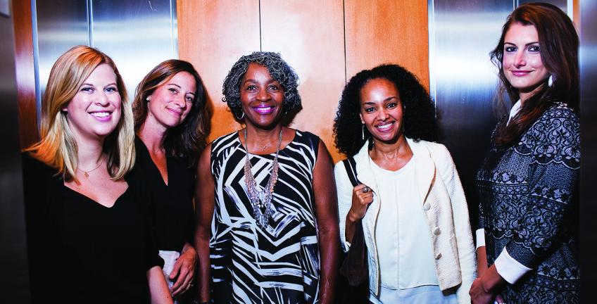 Five women stand, smiling, in an elevator