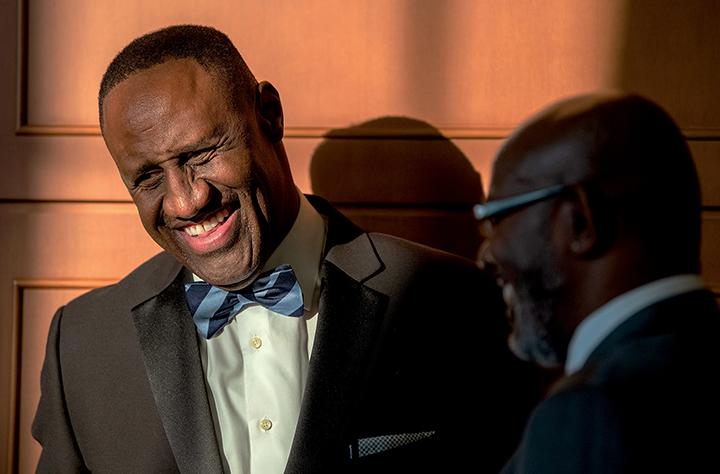 Ohio University Alumnus of the Year Dell Robinson, wearing a suit and blue striped bow tie, laughs and talks with a colleague 