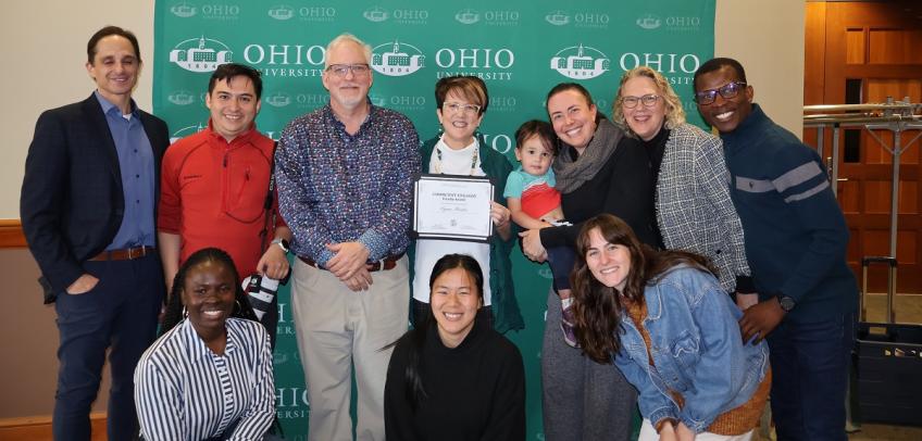 Lynn Harter is shown holding her award while surrounded by a group of supporters and collaborators