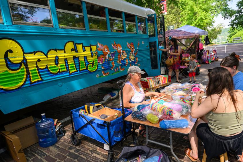 People of all ages sit at a craft table and stand nearby the Crafty Bus at the Juneteenth Celebration