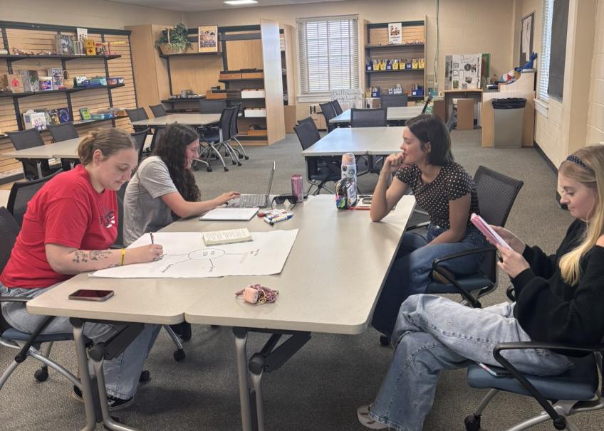 4 students in classroom, working on class projects at a table with four chairs