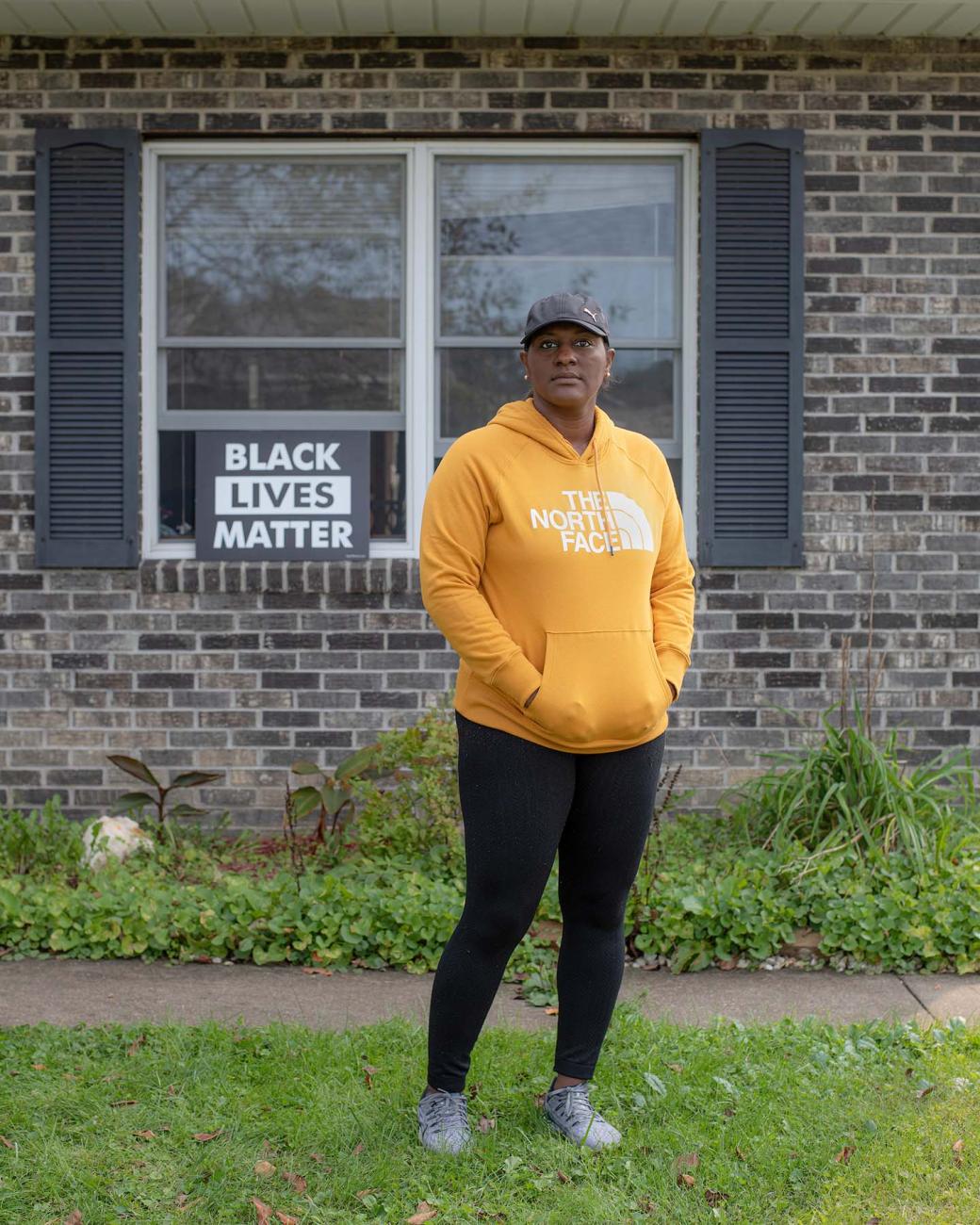 Jennifer Moore photographed outside her home, displaying a yard sign in the window