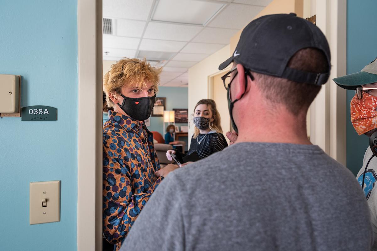 Student with mask on facing camera listens to person facing away from camera