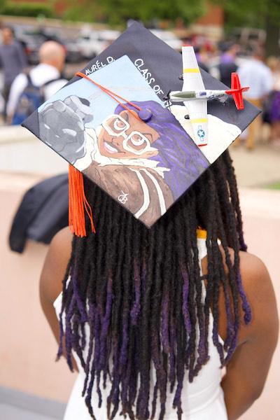 A young woman faces away from the camera, with her cap displayed with including a drawing of her as a pilot, a toy plane attached, with the words 