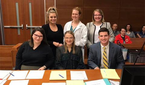 Group of students pose for a picture in a courtroom