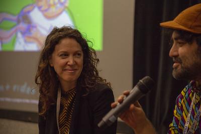 Two people sitting in front of a projector screen with one of them holding a microphone