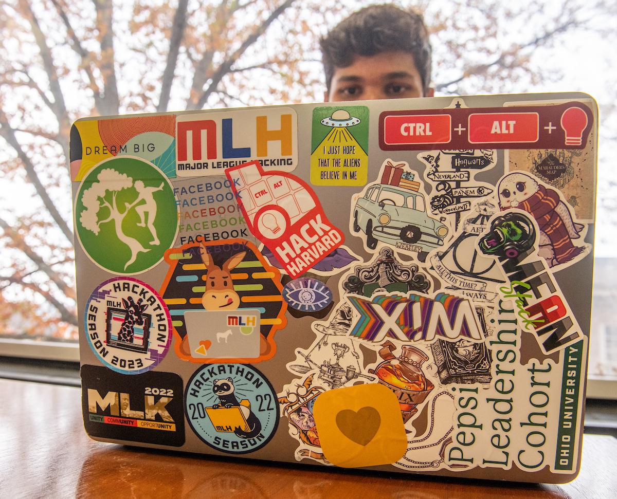 Parwinder Singh sits behind his laptop, with the back cover being covered in dozens of stickers.