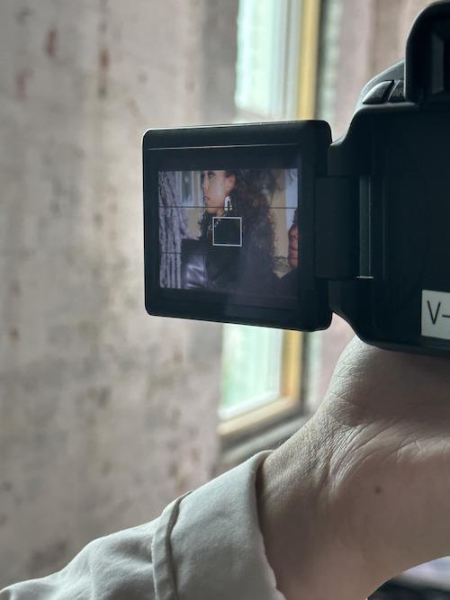 A close up of a student's hand with a camera in it, with the camera screen displaying a model about to get their photo taken.