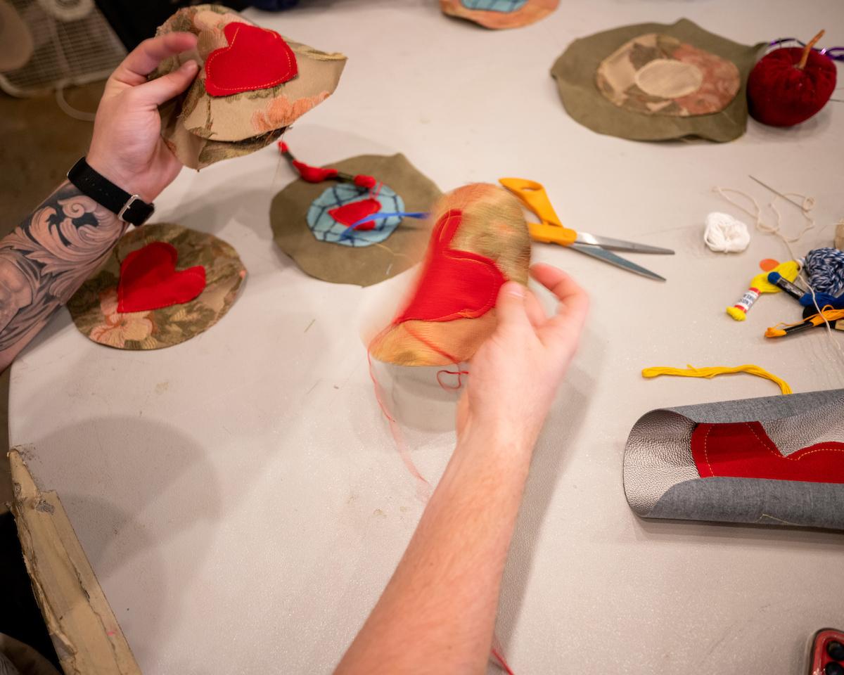 A student's hands are shown sewing costume parts for puppets for the Honey for the Heart parade