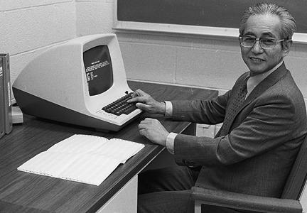 OHIO physics faculty Tomoyasu Tanaka sits at a desk with an early desktop computer
