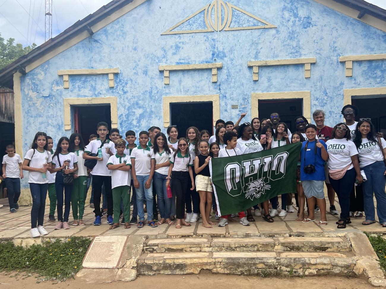 A group of children and OHIO students pose holding an Ohio University flag