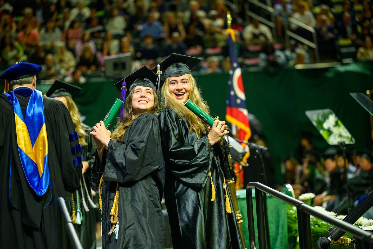 Two OHIO graduates in cap and gown celebrate after walking across the stage at Spring Commencement