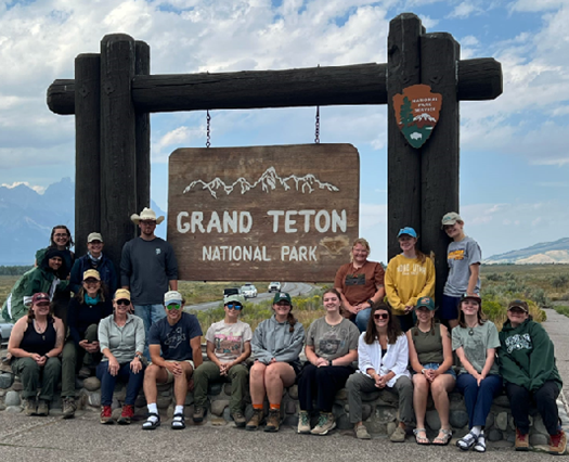 A group poses in front of the sign for Grand Teton National Park