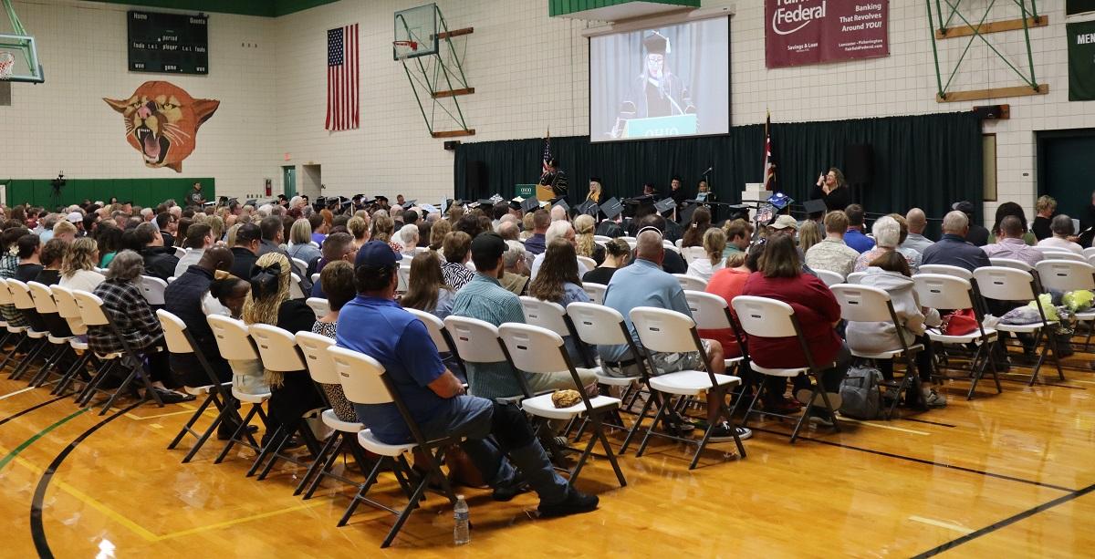 Family and friends sit in rows of chairs in the gymnasium and watch the Graduation Recognition Ceremony