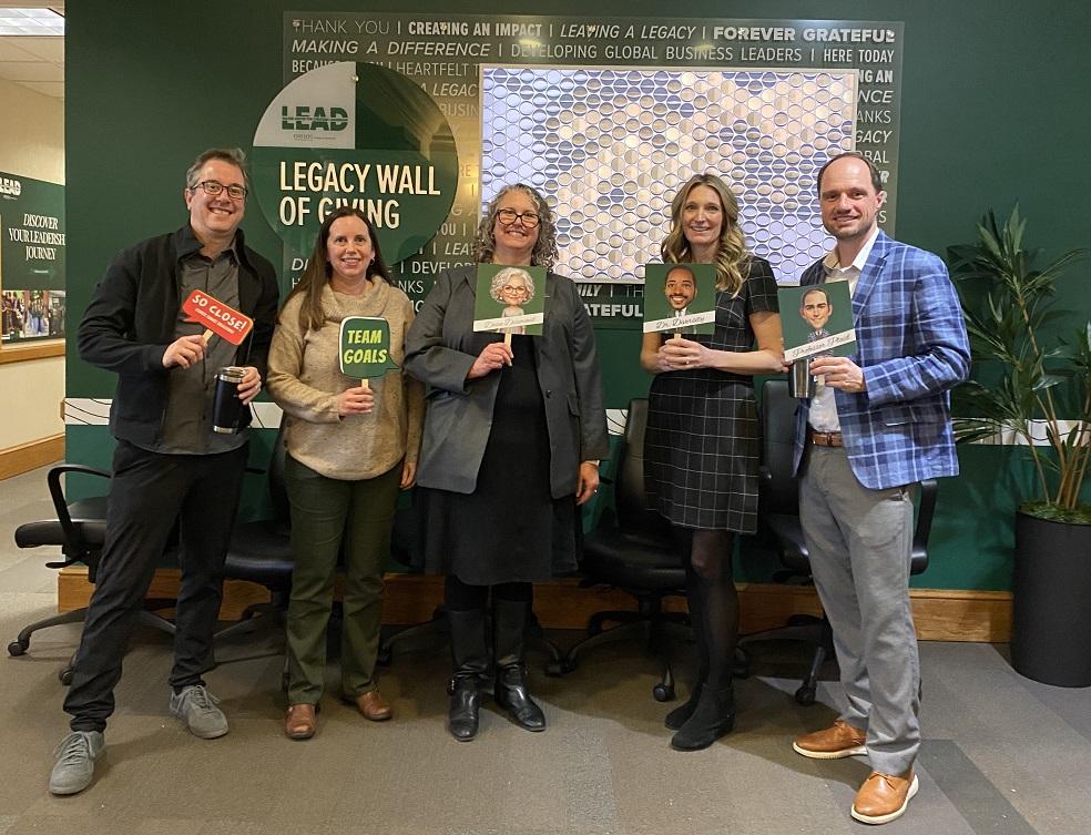 OHIO leaders hold signs showing their Clue game identities, while they stand in front of the Legacy Wall in Copeland Hall