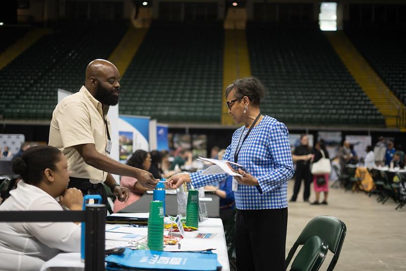 A man and a woman exchange business cards across a table at a booth at the Ohio Business Matchmaker event
